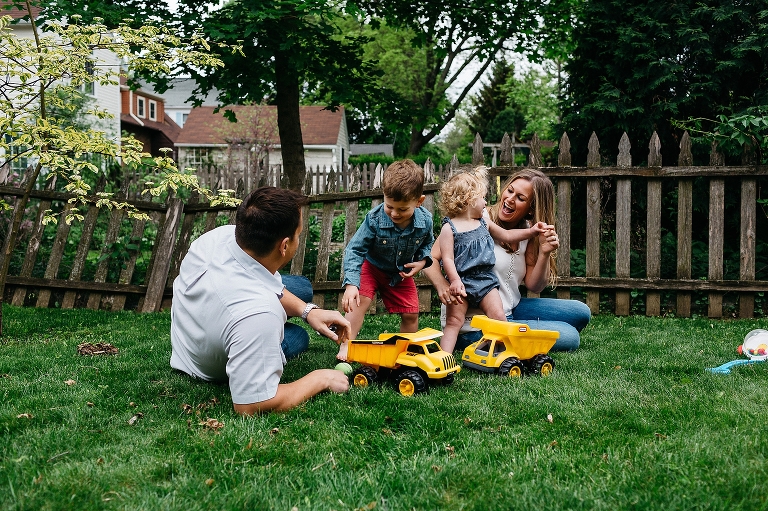 Father and mother sit in grass in backyard playing with son and daughter.