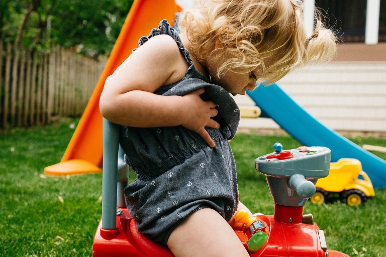 Young girl sitting on toy looking at her belly.