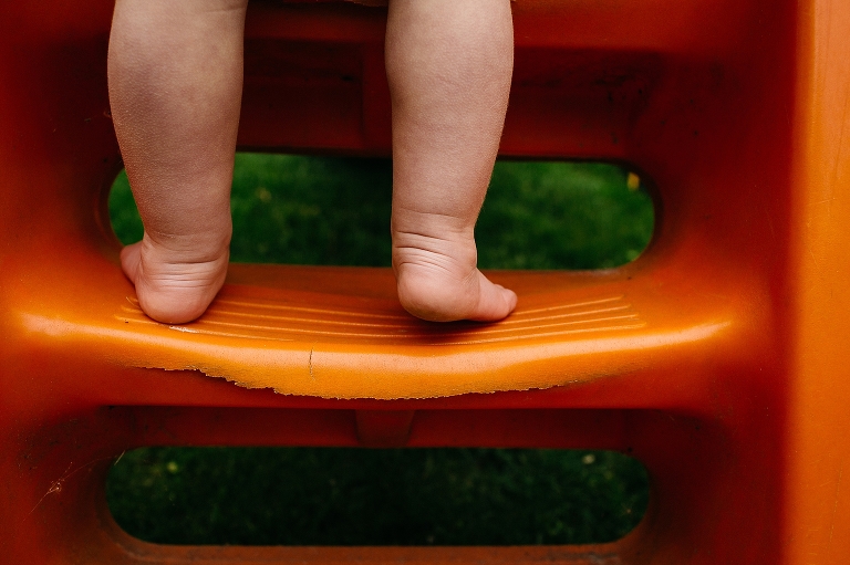 Young girl's baby feet with little wrinkles stand on orange play stairs.