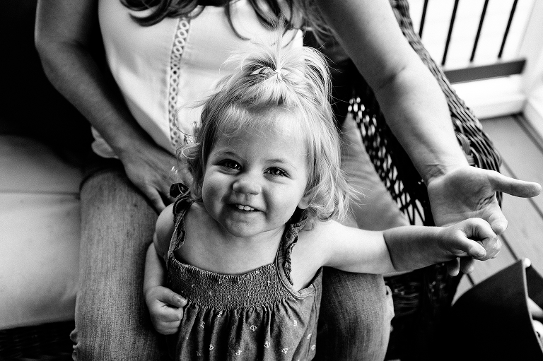 Black and white. Mother sits on chair with young daughter smiling for the camera.