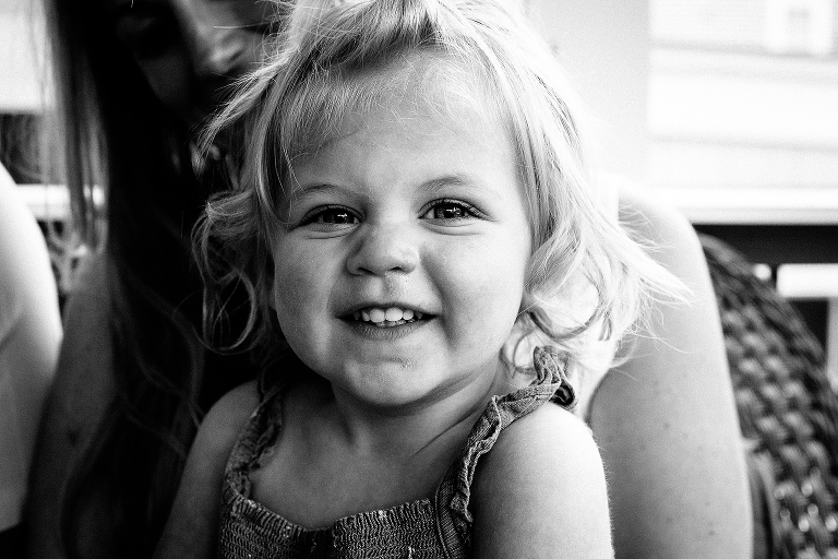 Black and white. Young girl smiles while sitting on mothers lap.