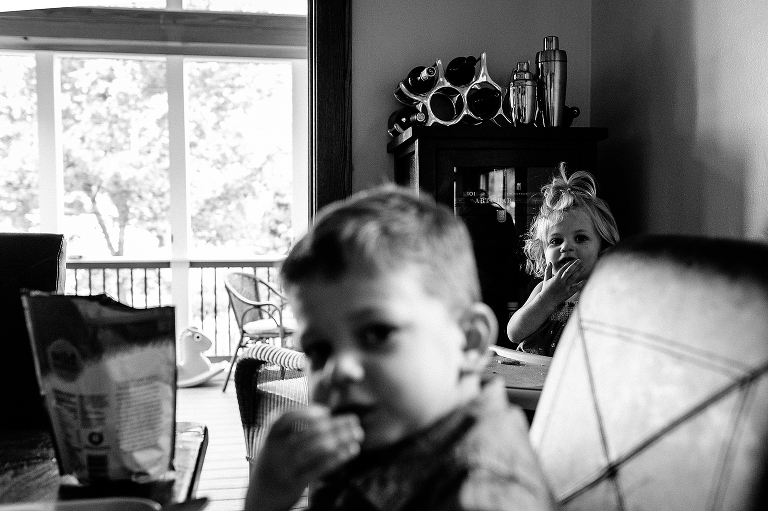 Black and white. Young brother and sister sit and eat a snack at dinner table.