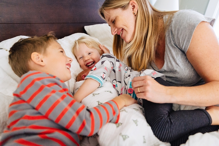 Mother, son, and daughter all lay in bed around sleeping newborn baby