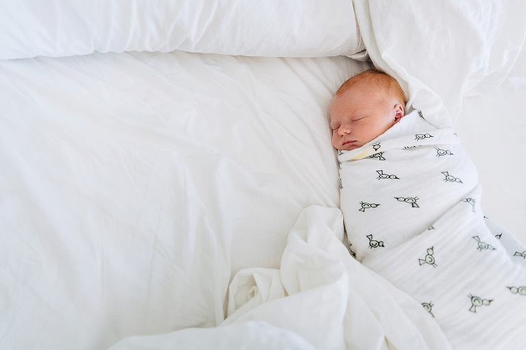Newborn baby swaddled in bird blanket sleeps on parents bed