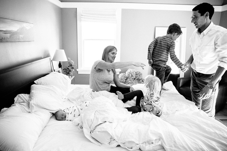 Black and white. Family of five sit on the bed together