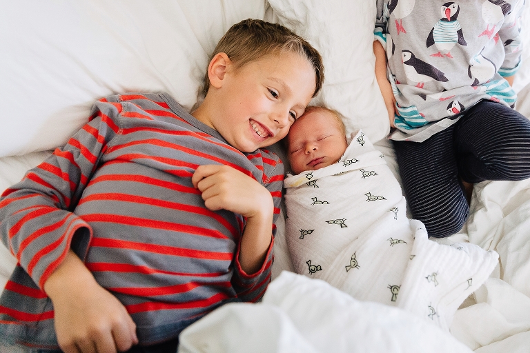 Young boy lays in bed with his new baby brother