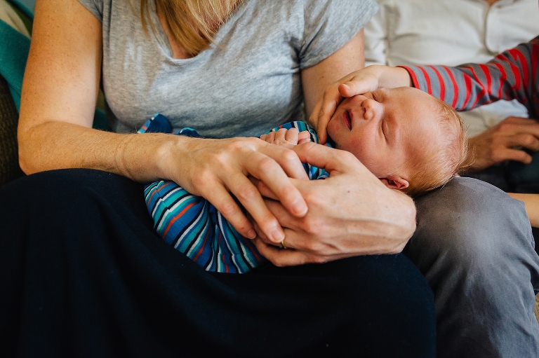 Mother holds newborn baby while son tickles the baby's chin
