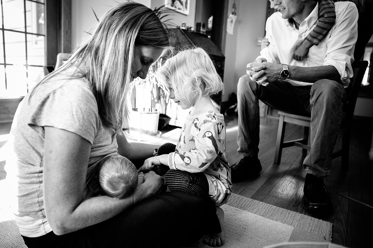 Black and white. Young girl watches her mother breastfeed newborn baby brother