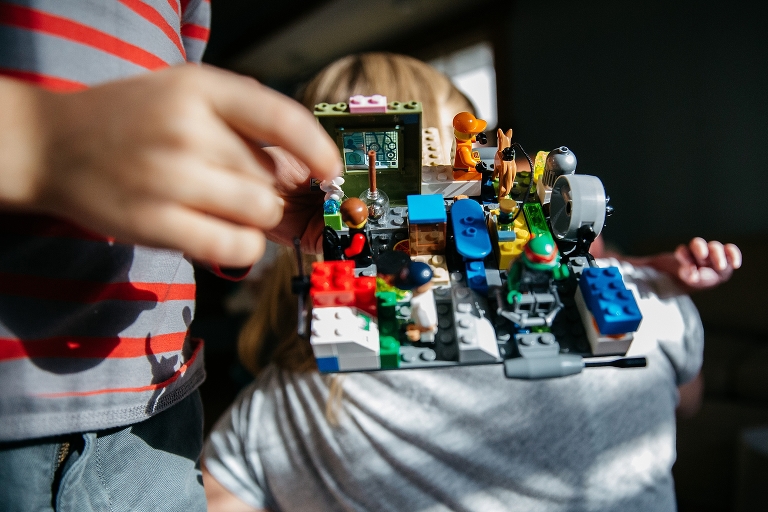 Young boy holds lego creation with newborn baby's hand in the background
