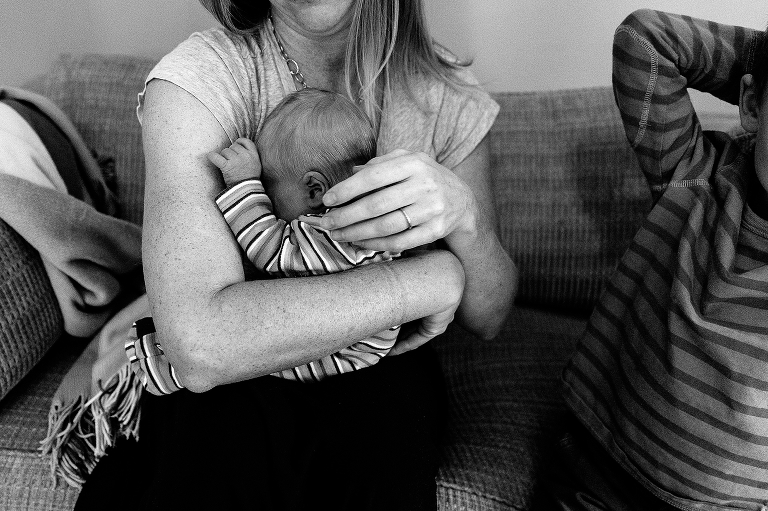 Black and white. Mother sits on couch holding newborn baby next to her son