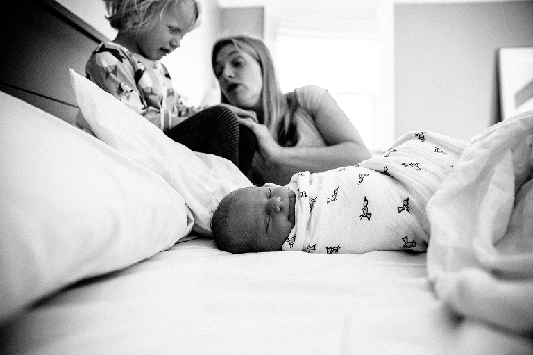Black and white. Mother talks to her daughter on the bed while newborn baby sleeps next to them