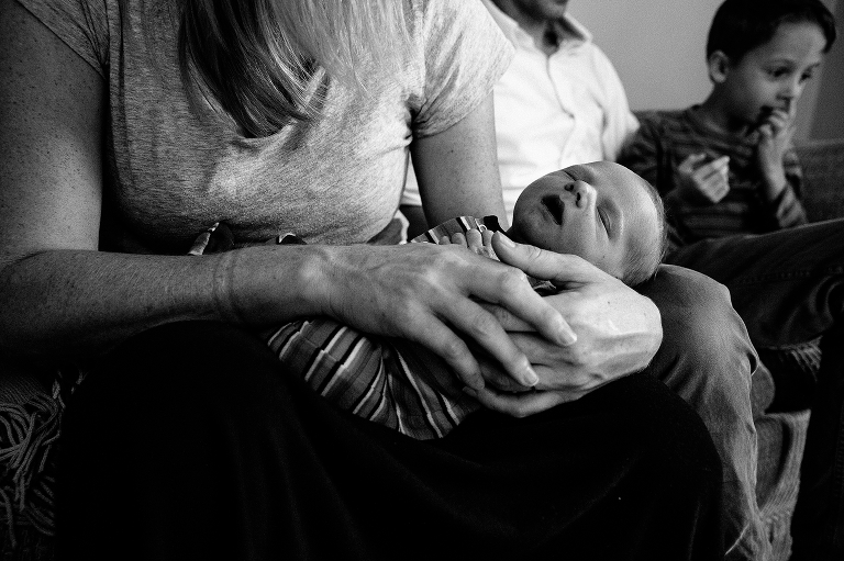 Black and white. Mother holds sleeping newborn baby on the sofa with father and son next to her
