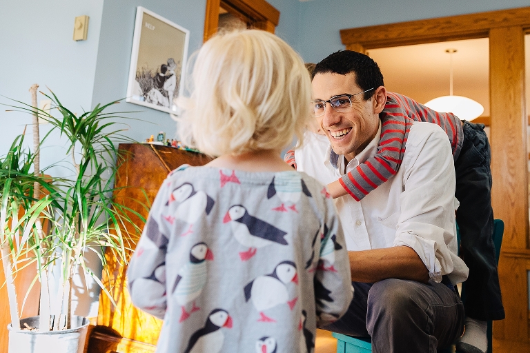 Father sitting in chair with son on his back looks at his daughter