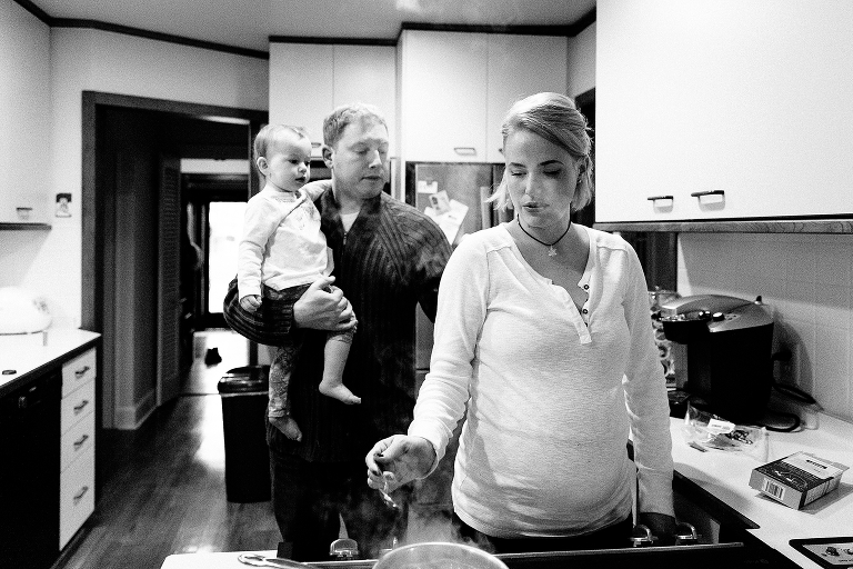 Black and white, Father hold baby in kitchen while mother cooks on the stove 