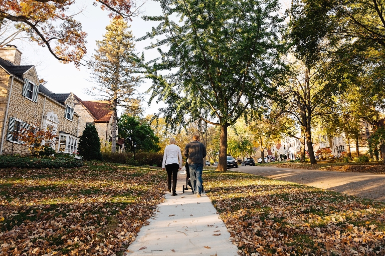 Family walks up sidewalk pushing baby in the stroller on a fall day
