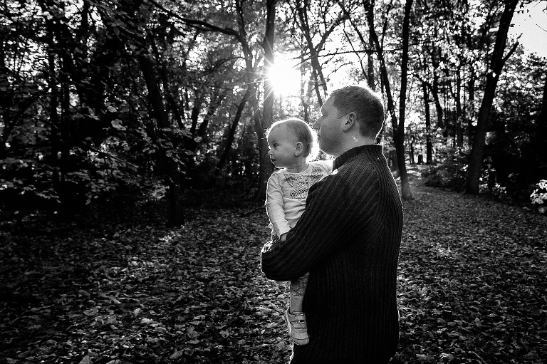 Black and white, Father holds baby daughter at park with sun shining through the trees