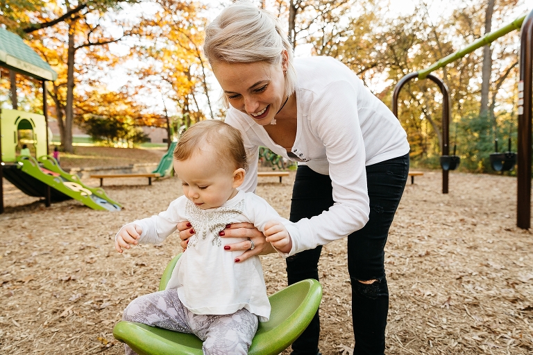Mom helps baby sit on play set at park