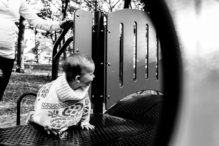 Black and white, Mother follows behind baby crawling up play structure at the park