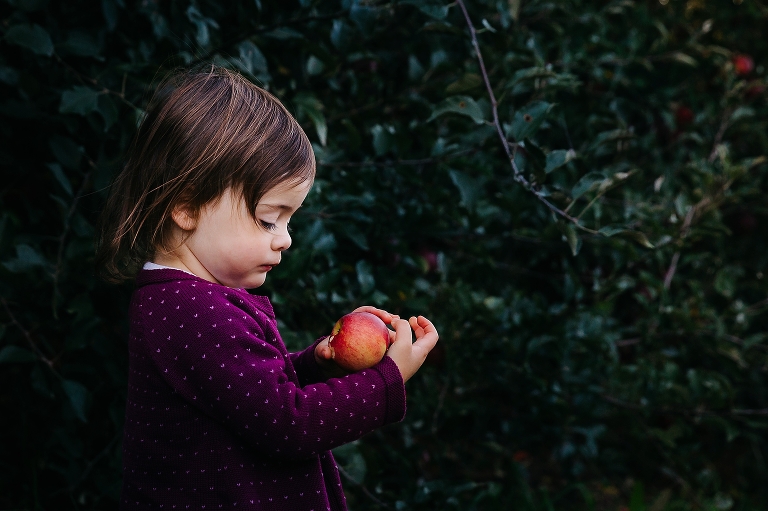 Toddler girl stands outside holding and looking at red apple