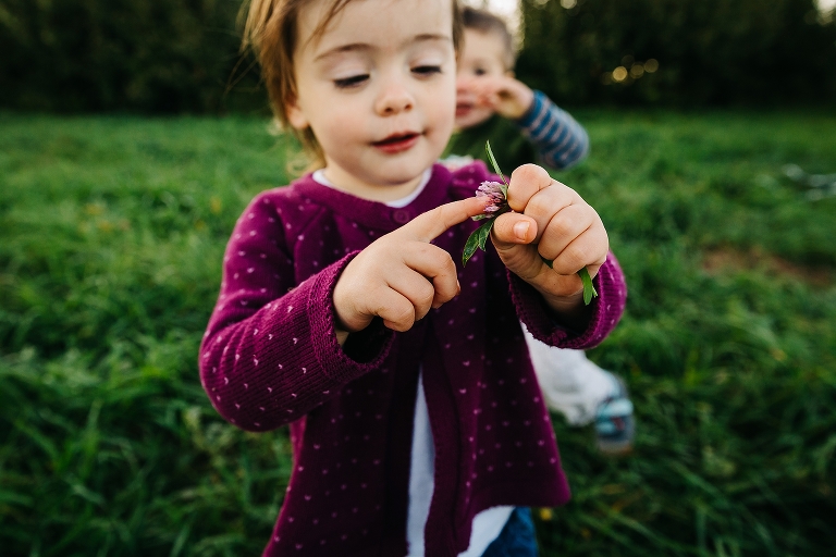Two toddlers walk through the grass holding dandelion leaves
