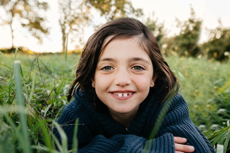 Young girl lays in grass smiling.