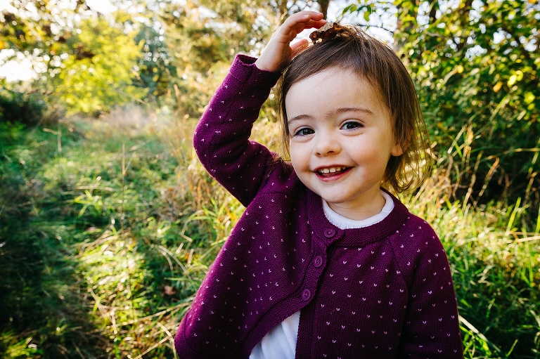 Young girl smiles standing outside in a field of grass with trees.