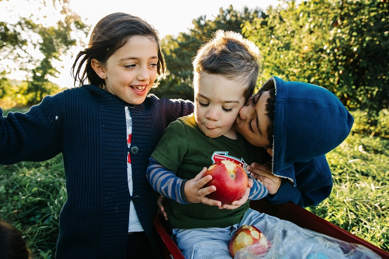 Children sit together in a red wagon eating apples at apple orchard.