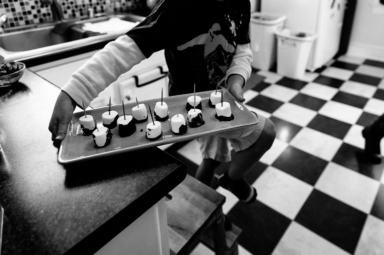 Black and white. Boy in kitchen cary's tray of chocolate covered marshmallows.