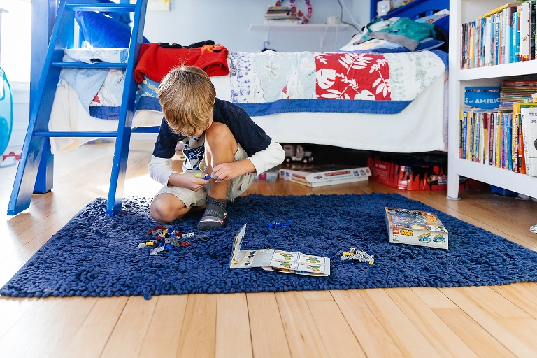 Boy knelling on rug in bedroom assembles new star wars lego character.