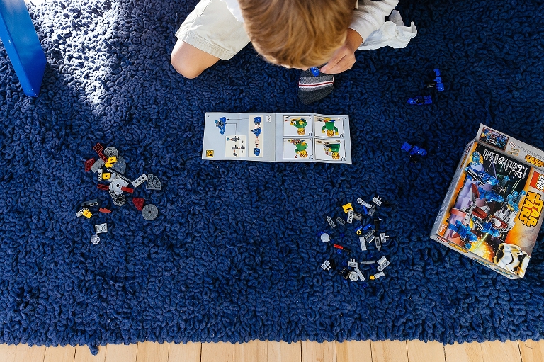 Boy knelling on rug in bedroom assembles new star wars lego character.