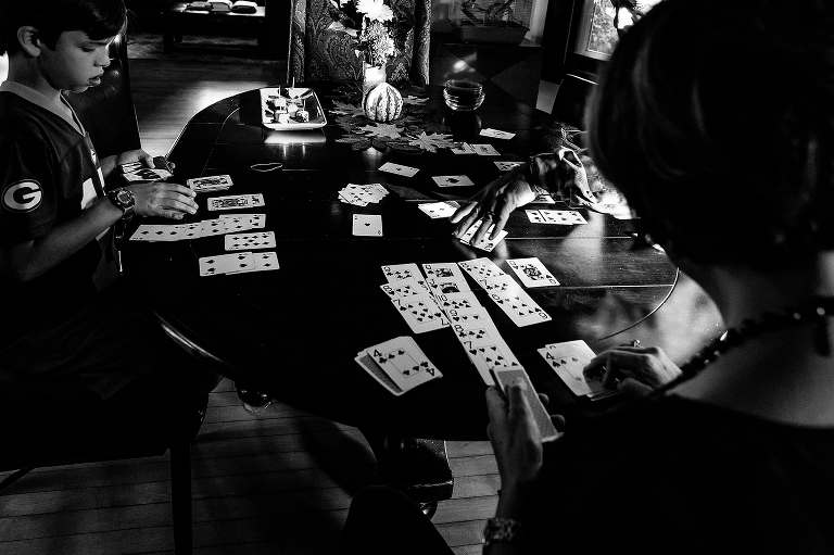 Black and white. Boy plays card game on table with family