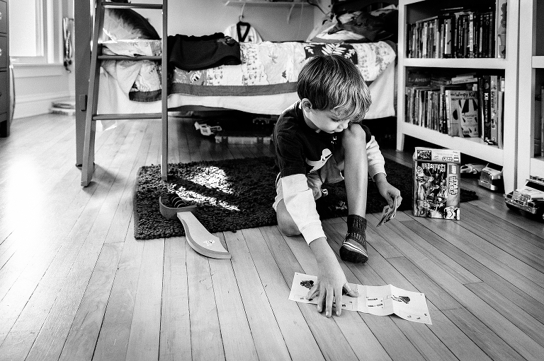 Black and white. Young boy in bedroom picks up lego instructions. 