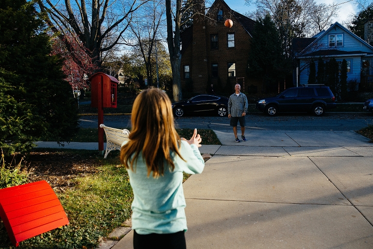 Father and daughter play football outside in driveway.