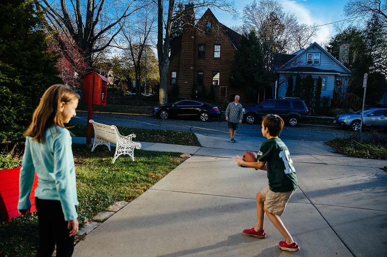 Father, daughter, and son play football outside in driveway.