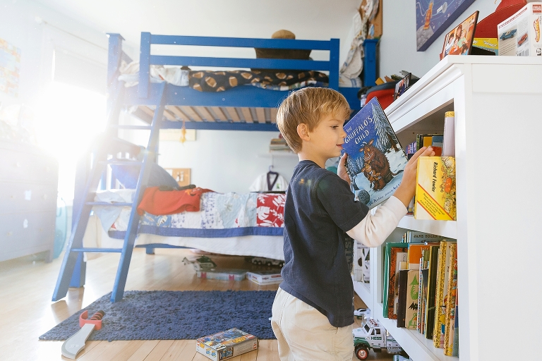 Young boy in bedroom pulls picture book out of bookshelf