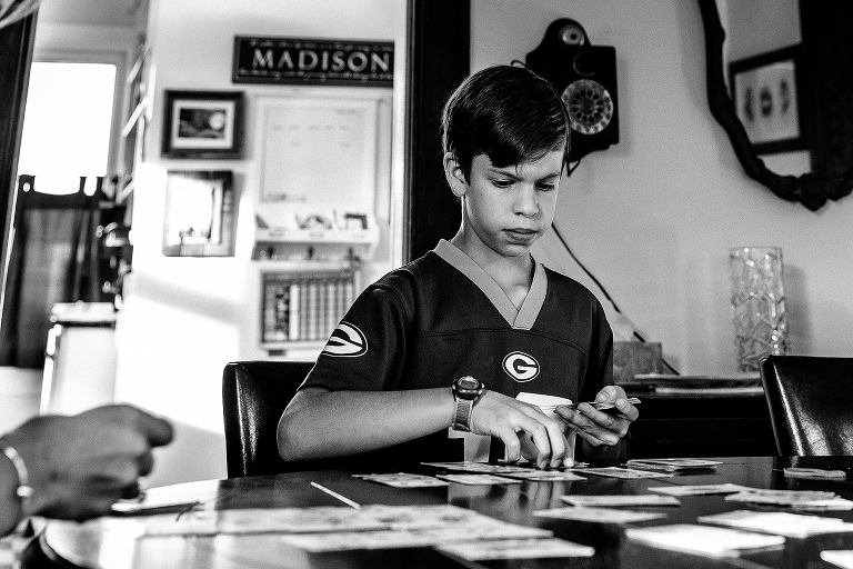 Black and white. Boy plays card game on table with family
