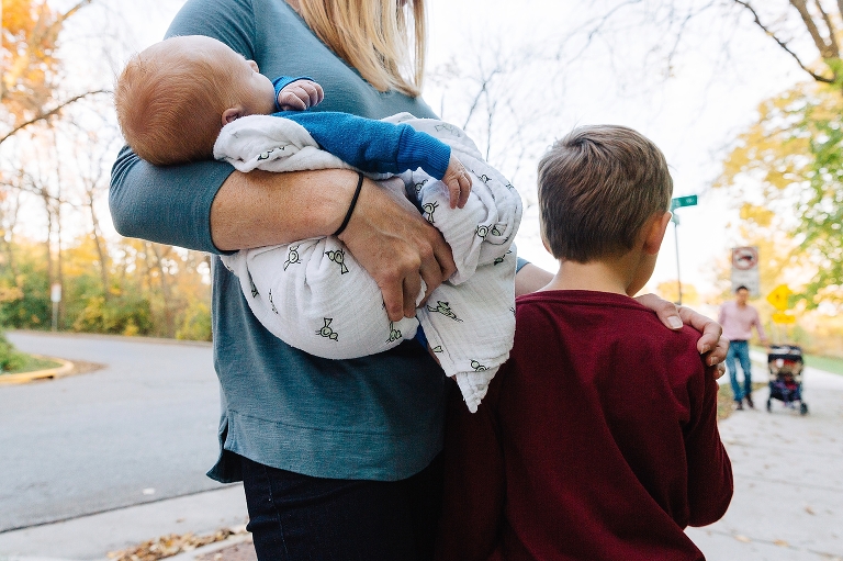 Mother holds newborn and son while father and daughter push a stroller outside