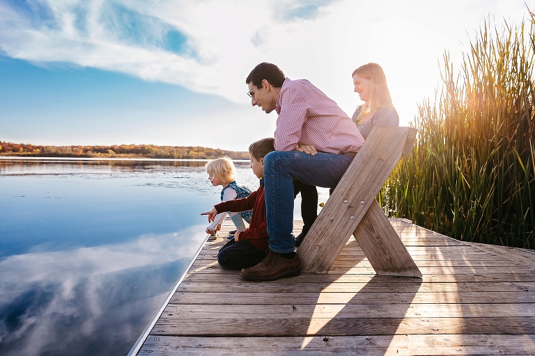 Family sitting together on a dock bench look into the lake