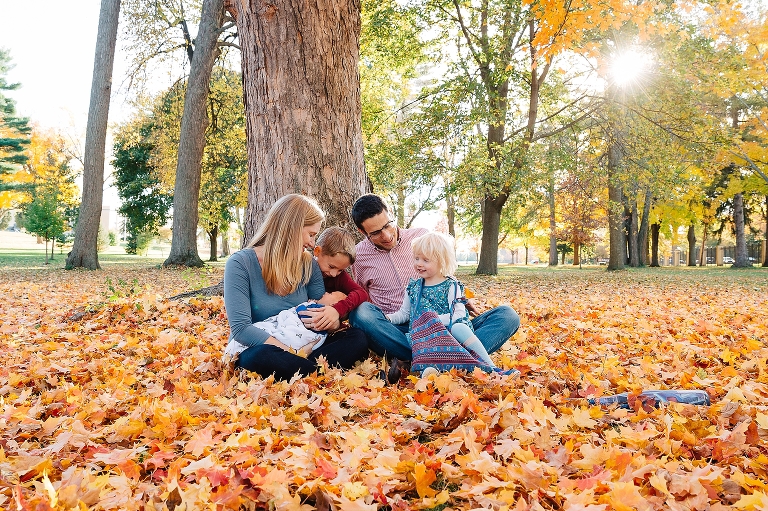 Family of five sits outside by a tree with fallen orange leaves all around them