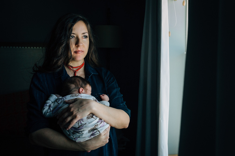 Mom sits in window light holding her newborn baby.