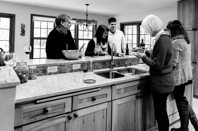 Black and white. Family stands around the kitchen together.