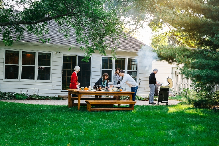 Family stands outside setting the table and grilling
