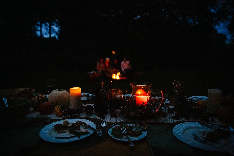 Candles on dinner table at evening with family sitting around fire pit in the background