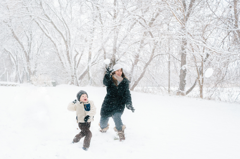 Mom throws snowballs with young son in a snowstorm.