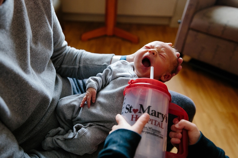 Father holds crying newborn baby while brother holds water cup