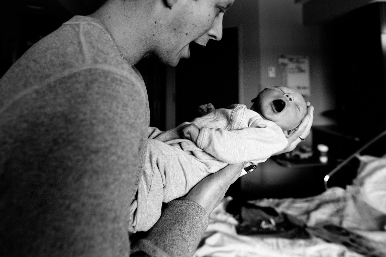 Black and white, Father holds and clams crying newborn baby in hospital.