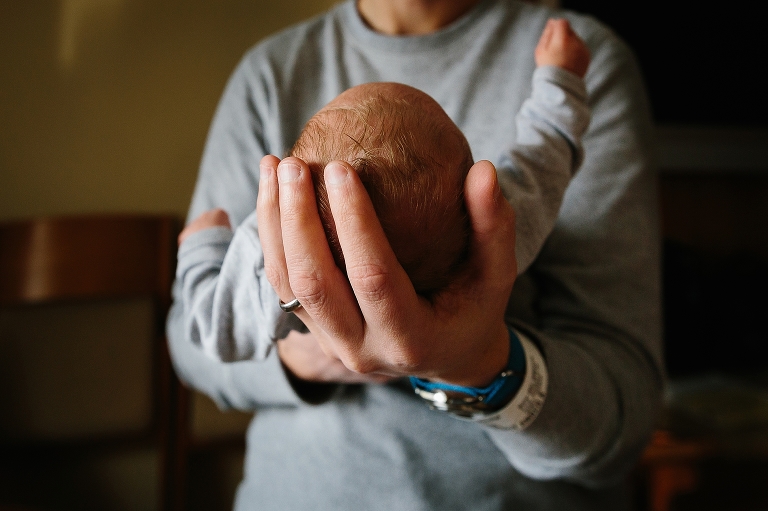 Father holds out newborn cradling baby's head in hospital.
