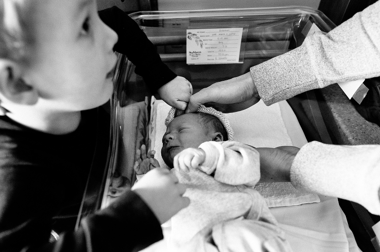 Black and white, Young boy helps put hat on newborn baby boy.