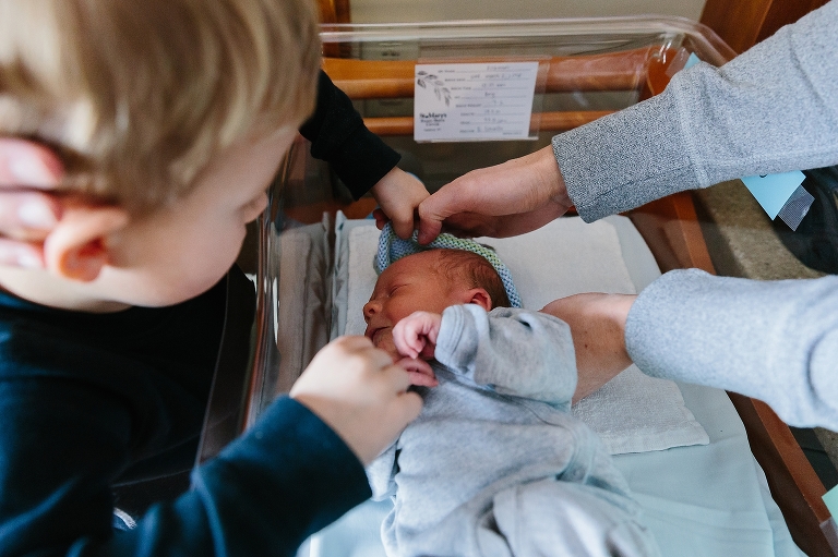 Son helps put hat on his new baby brother in hospital.