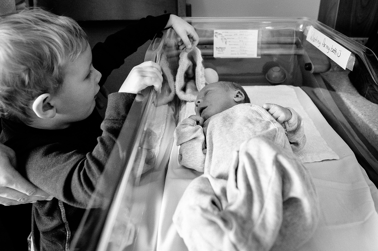 Black and white, Toddler watches baby brother sleep in hospital.